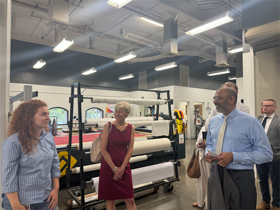 Rep Ross standing with representatives of the institute talking in front of rolls of fabric